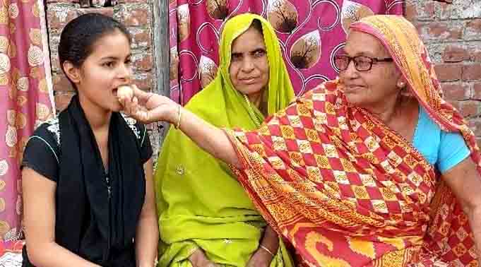 दसवीं की परीक्षा में अपने जिले में सर्वोच्च स्थान पाने वाली प्रियांशु को मिठाई खिलाती उसकी दादी