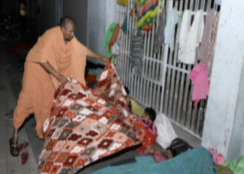 फुटपाथ पर लेटे व्यक्ति को कंबल ओढ़ाते एक साधु